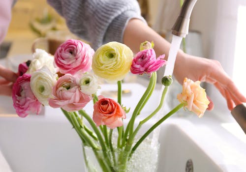 Water flows from a kitchen faucet into a vase, containing a dozen vibrant mixed flowers
