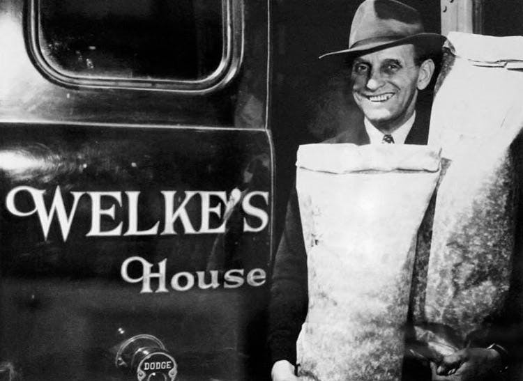 A grinning Bill Welke hauls two bags of seed near the painted door of a delivery vehicle